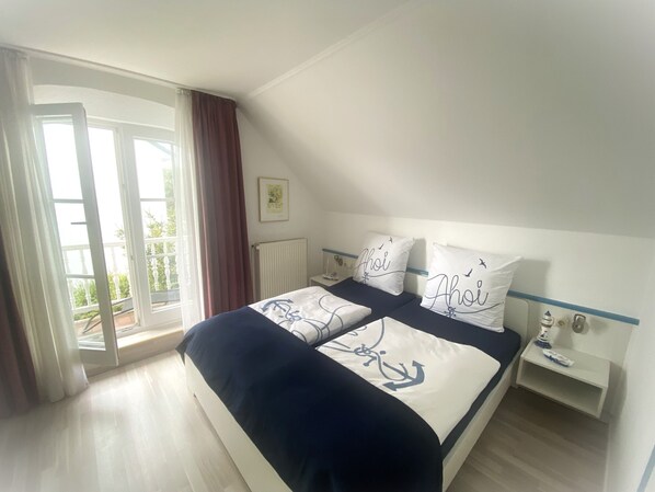 A bedroom with a bed, a nightstand, a window with curtains, and a radiator.