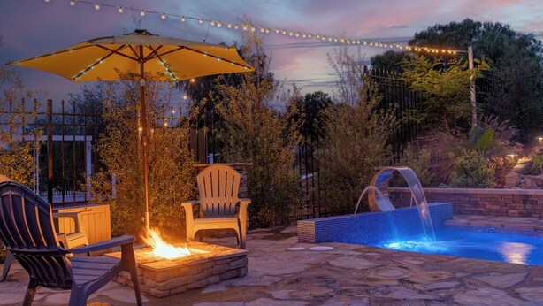 Eine Terrassenausstattung mit einem Steinkamin, zwei Adirondack-Stühlen, einem gelben Sonnenschirm, einem kleinen Pool mit Wasserfall und Lichterketten.