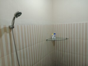 Een douche met een handdouche en een glazen plank met toiletartikelen.