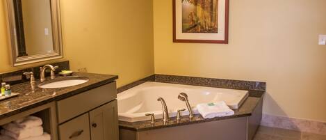A bathroom with a double sink, a large bathtub, and a framed picture on the wall.