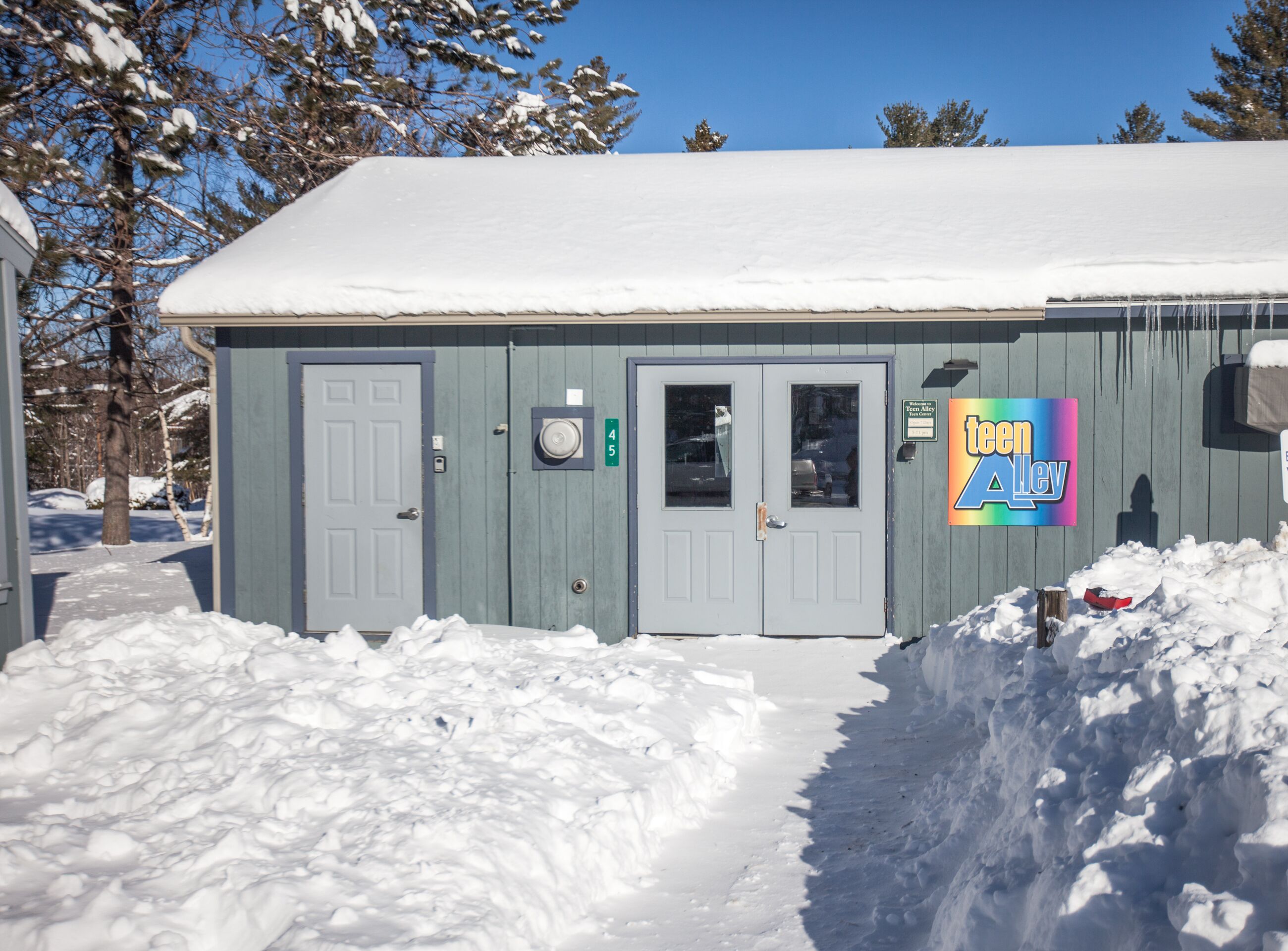 A small, single-story building with a snow-covered roof and a sign reading "Teen Valley."