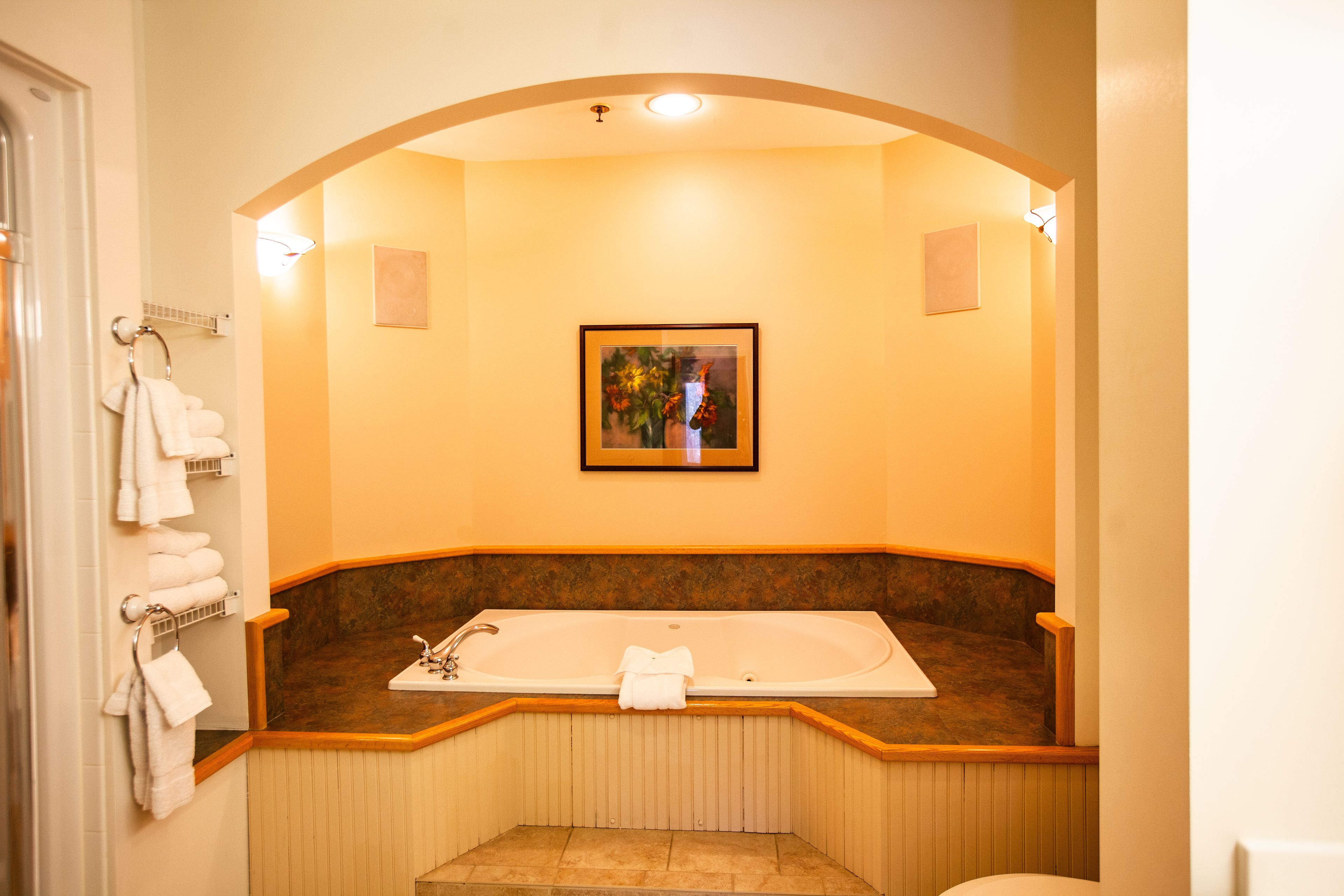 A bathroom with a large bathtub, a framed picture on the wall, and towels hanging on a rack.