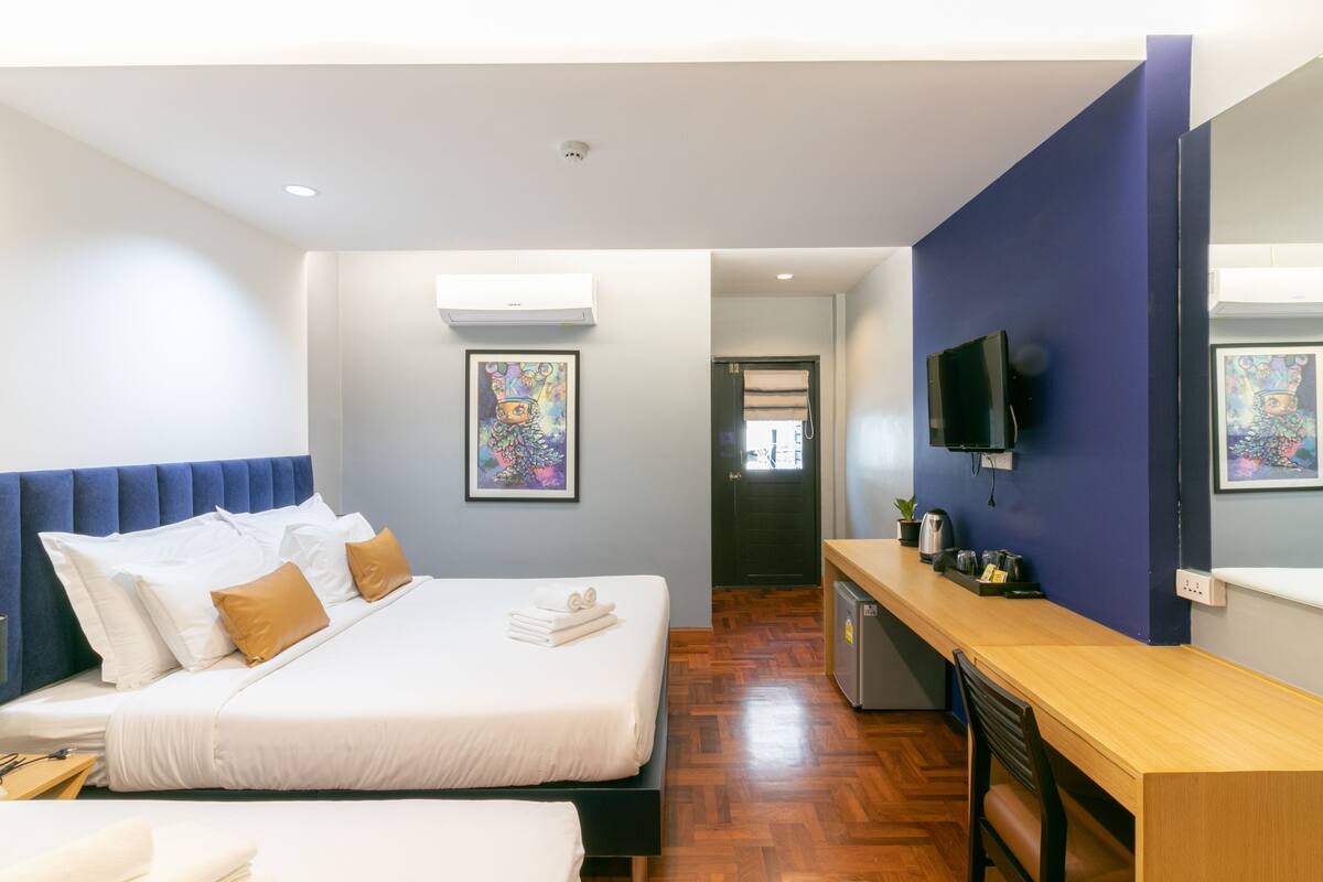 A hotel room with two beds, a desk, a TV, and artwork on the walls.