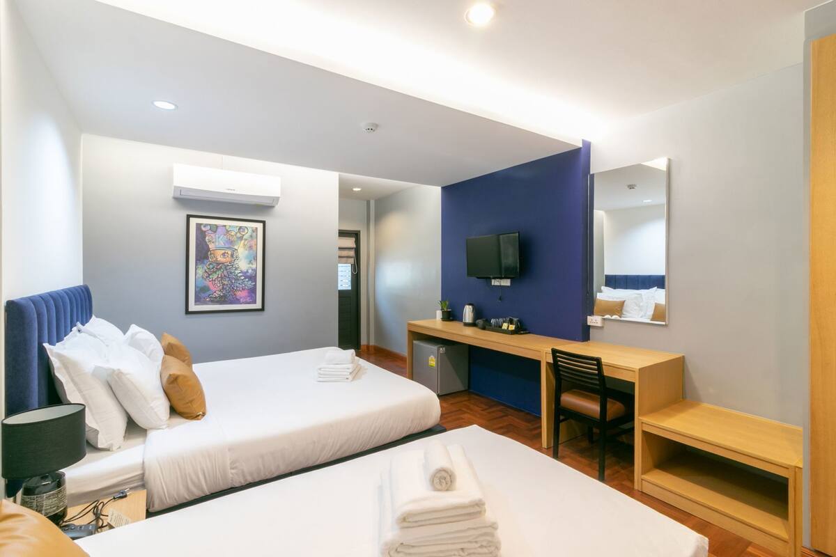 A hotel room with two beds, a desk, a TV, and a mirror.