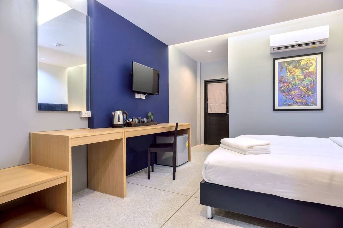 A hotel room with a bed, a desk, a chair, a television, and an air conditioning unit.