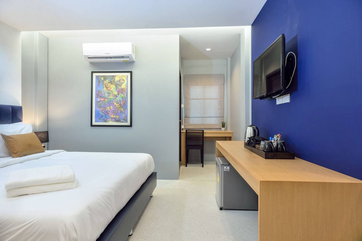 A hotel room with a bed, a desk, a TV, and a small kitchenette.