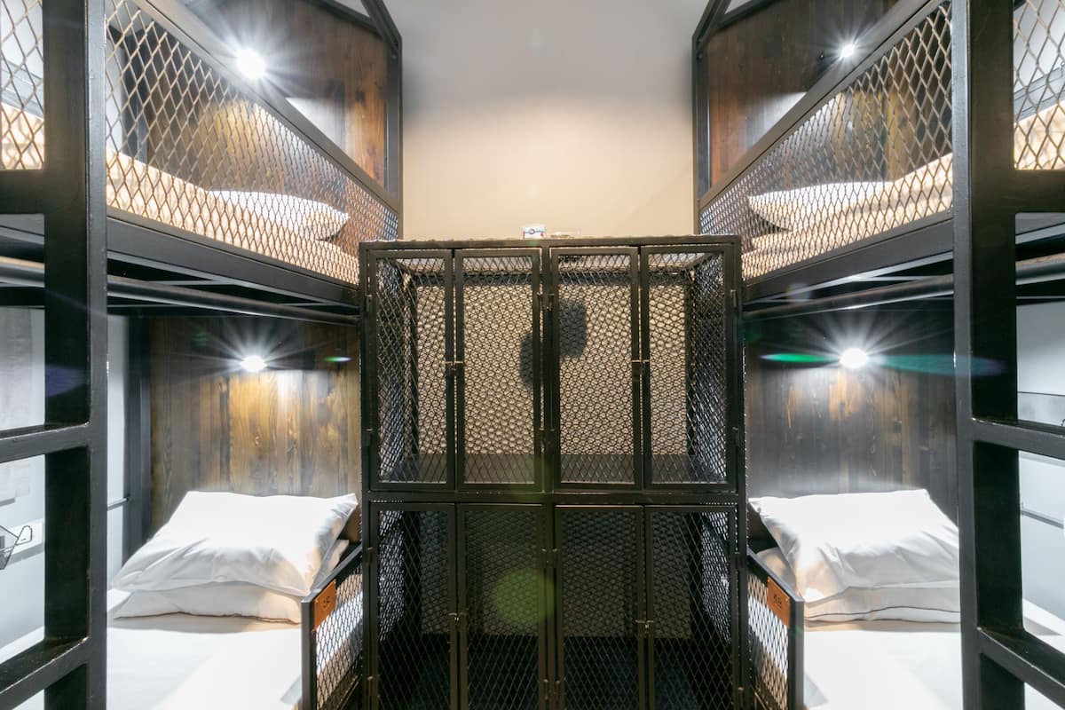 A bunk bed room with a central metal partition, wooden walls, and a window with sunlight streaming in.