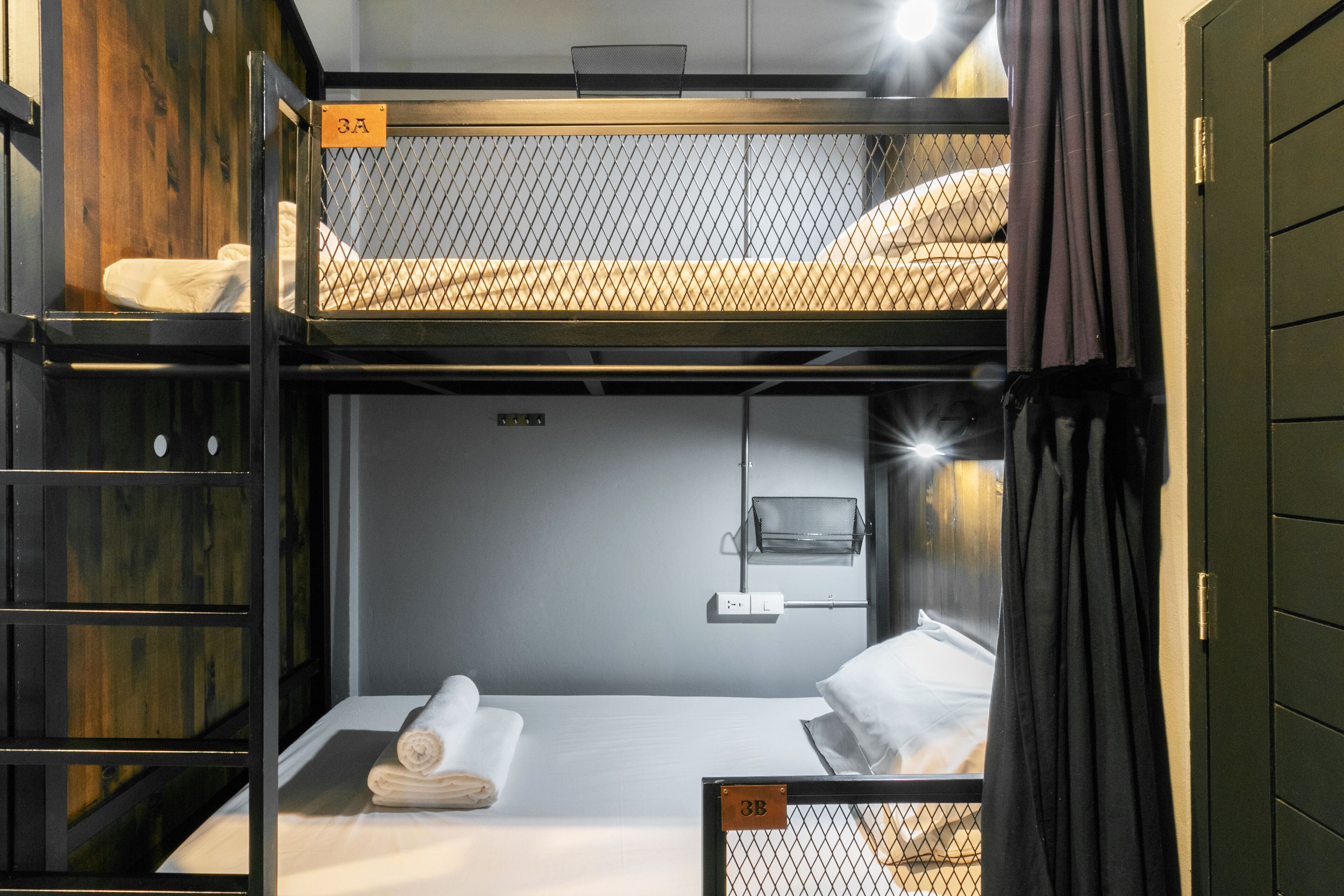 A bunk bed room with a wooden headboard, a small shelf, and a bedside table with a lamp.