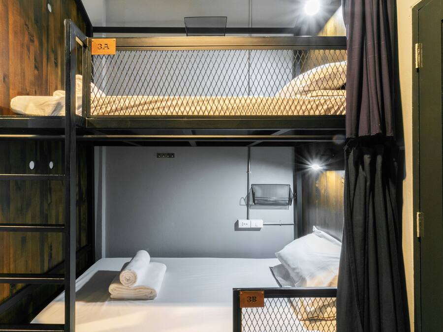 A bunk bed room with a wooden headboard, a small shelf, and a bedside table with a lamp.
