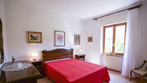 Ein Schlafzimmer mit einem hölzernen Bett, einem Nachttisch mit Lampe, einem Schminktisch und einem Fenster mit Vorhängen.
