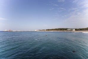 Vista costeira com um farol, praia e edifícios ao longe.