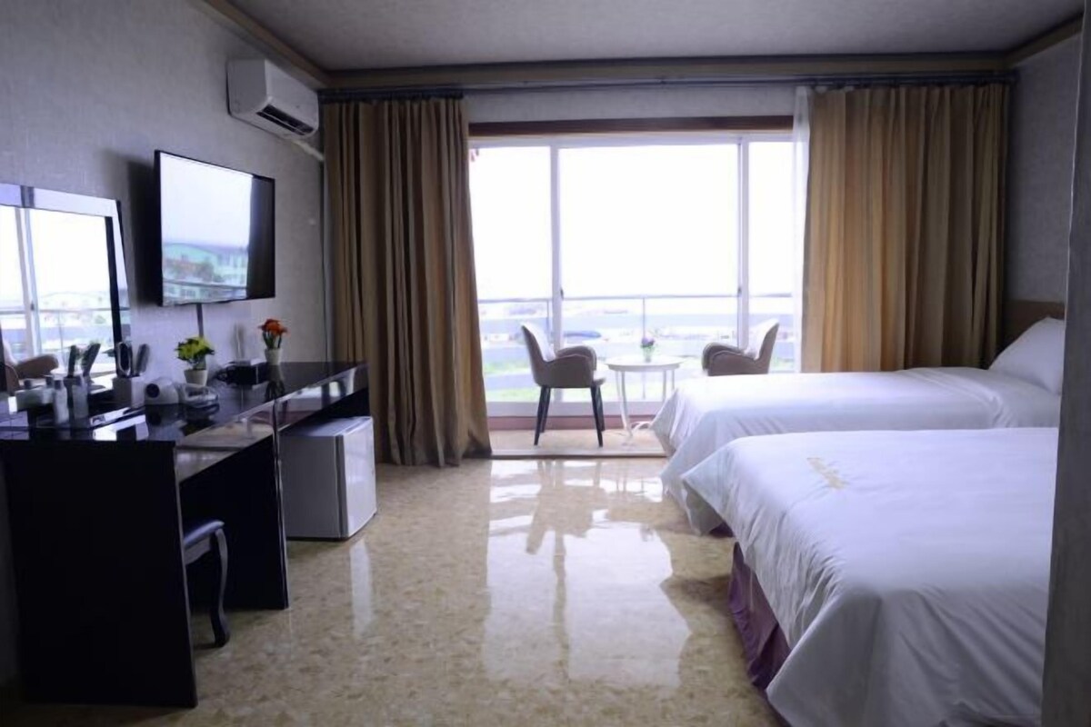 A hotel room with a desk, two beds, a TV, and a view of the city.