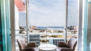 Un balcón con dos sillones de cuero y una mesita, con vistas a la costa, edificios y el mar.