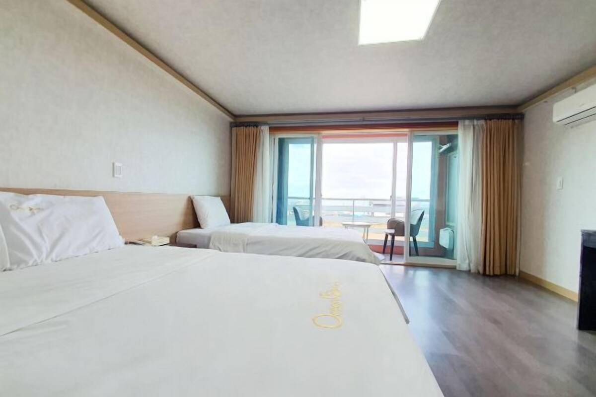 A hotel room with two beds, a balcony, and a view of the sea.