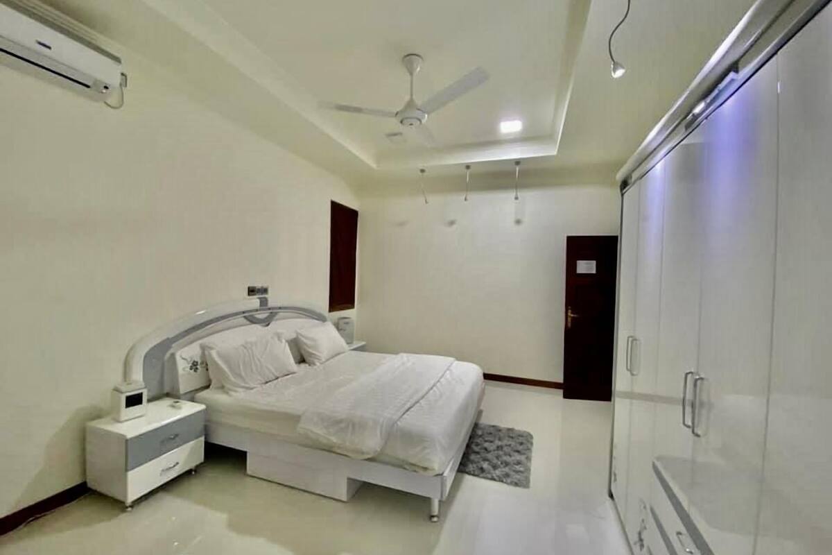 Une chambre à coucher comprenant un lit, une table de chevet, une commode, une armoire, un ventilateur de plafond et un appareil de climatisation.