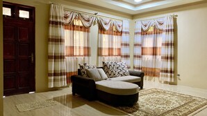 A living room with a sofa, patterned curtains, a wooden door, and a ceiling fan.