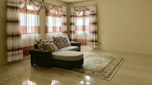 A spacious living room with a sofa set, a rug, and curtains.