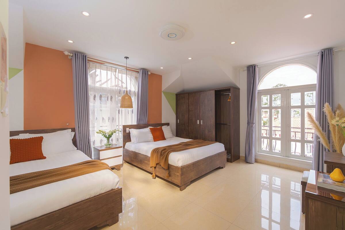 A hotel room with two beds, a wardrobe, a vanity with a mirror, and a large window with curtains.