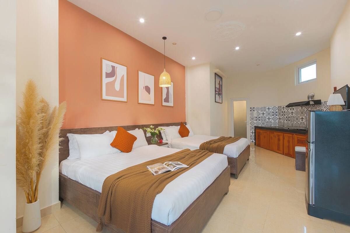 A hotel room with two beds, a kitchenette, and a bathroom.