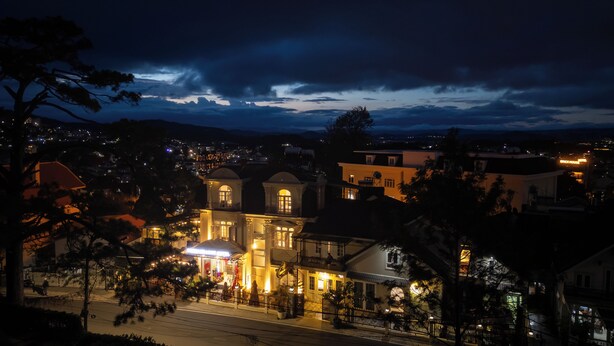 A hotel with multiple stories, a balcony, and a view of the surrounding town at night. - Green Meadow Central Đà Lạt - O'TEL (Xuan Huong - Da Lat)