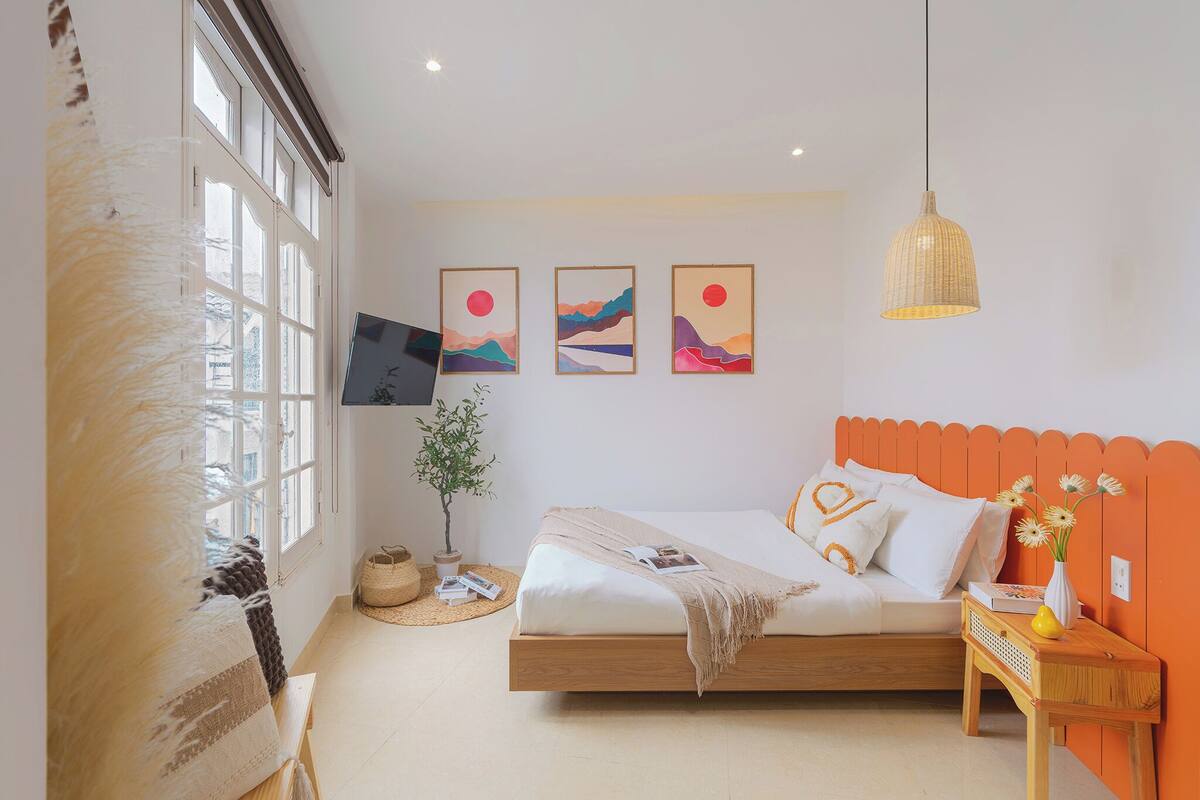 A bedroom with a bed, a bedside table, a hanging light, and wall art.