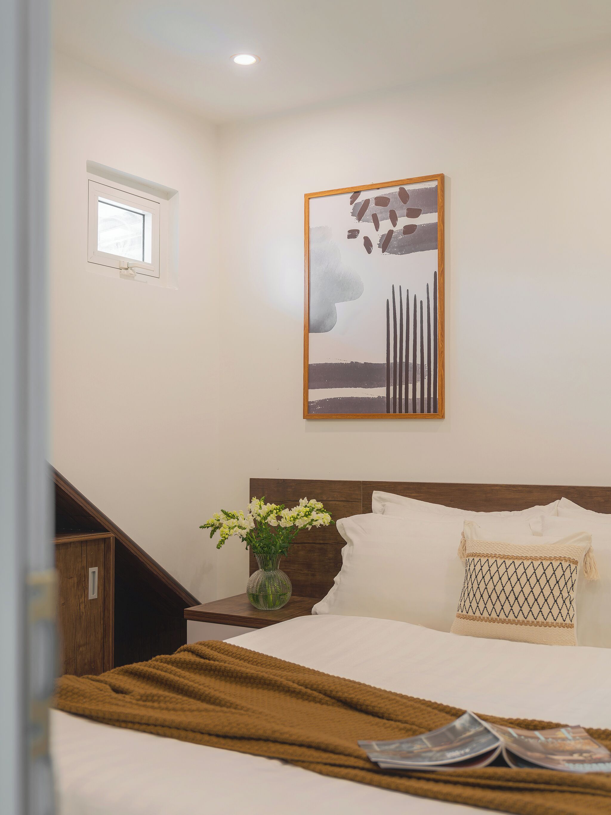 Ein Schlafzimmer mit Bett, Nachttisch, Fenster und Wandbild.