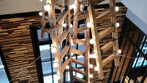 A high ceiling with exposed wooden beams and hanging light bulbs, a concrete floor, and a view of the outside through large windows. - Just Sleep Sanchong (New Taipei City)