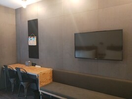 Una habitación moderna con una mesa de madera, sillas negras, un banco y un televisor montado.