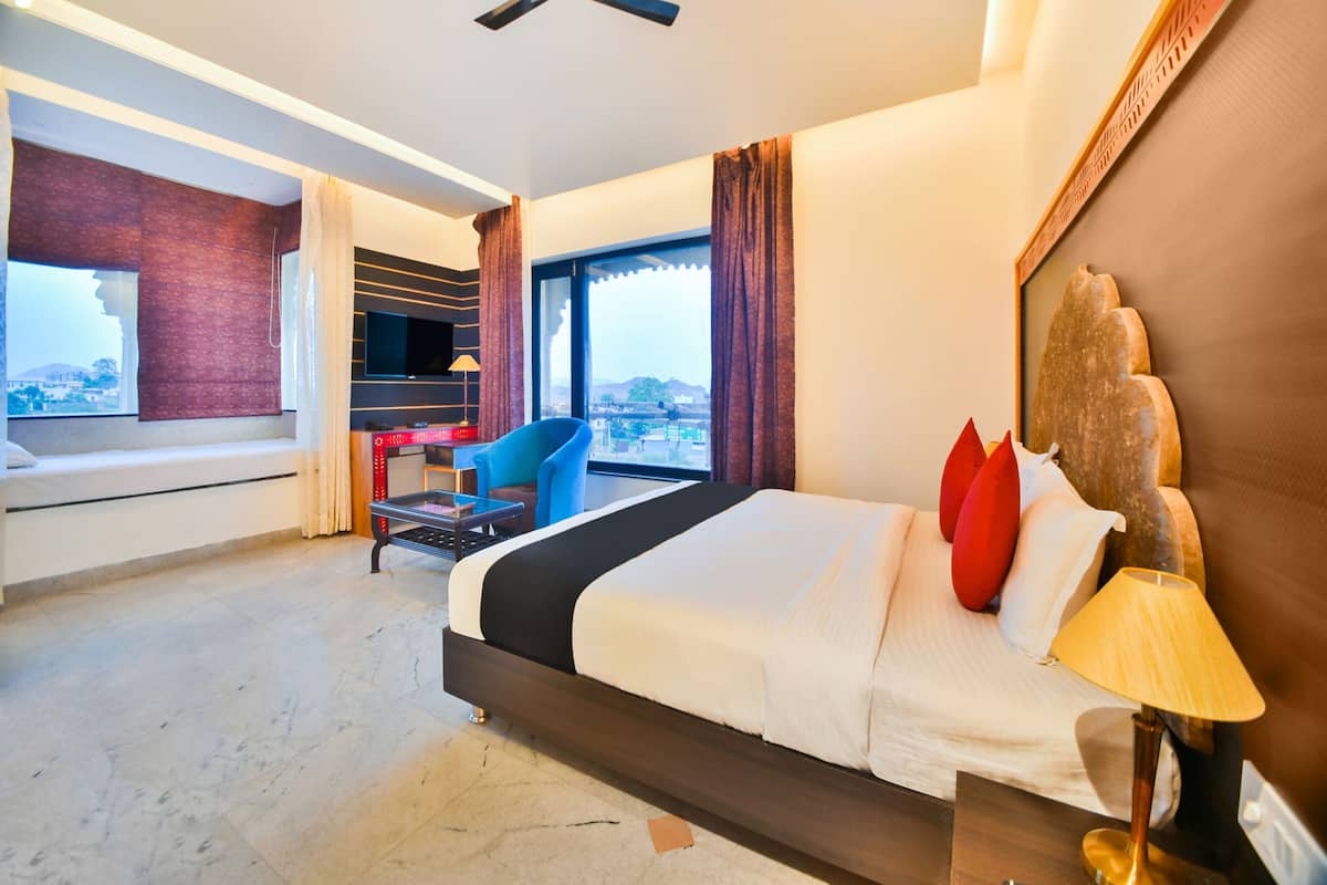 A hotel room with a bed, a desk, a chair, a TV, and a view of the city.