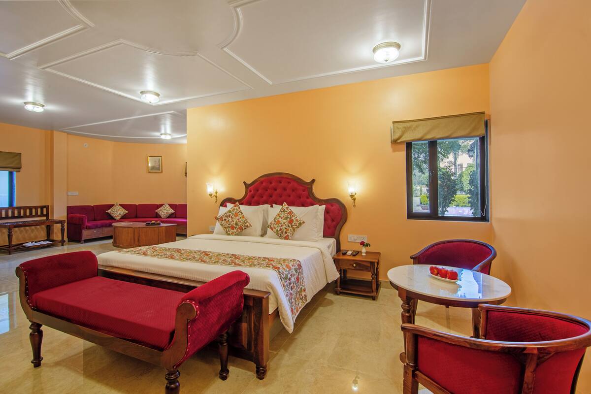 A hotel room with a large bed, a red armchair, a small table, and a sofa.