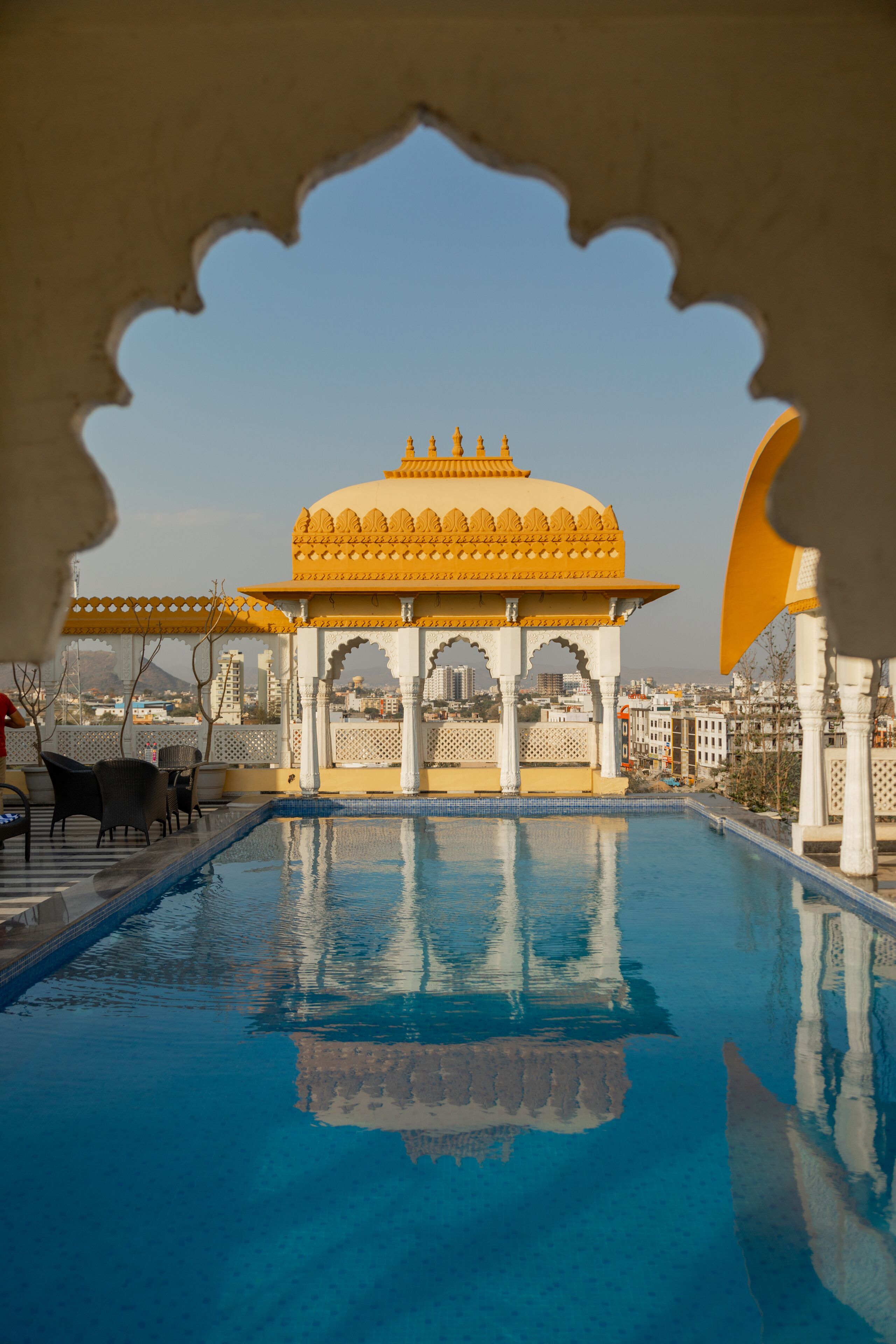 A pool area with a yellow pavilion, white arches, and a clear blue sky.