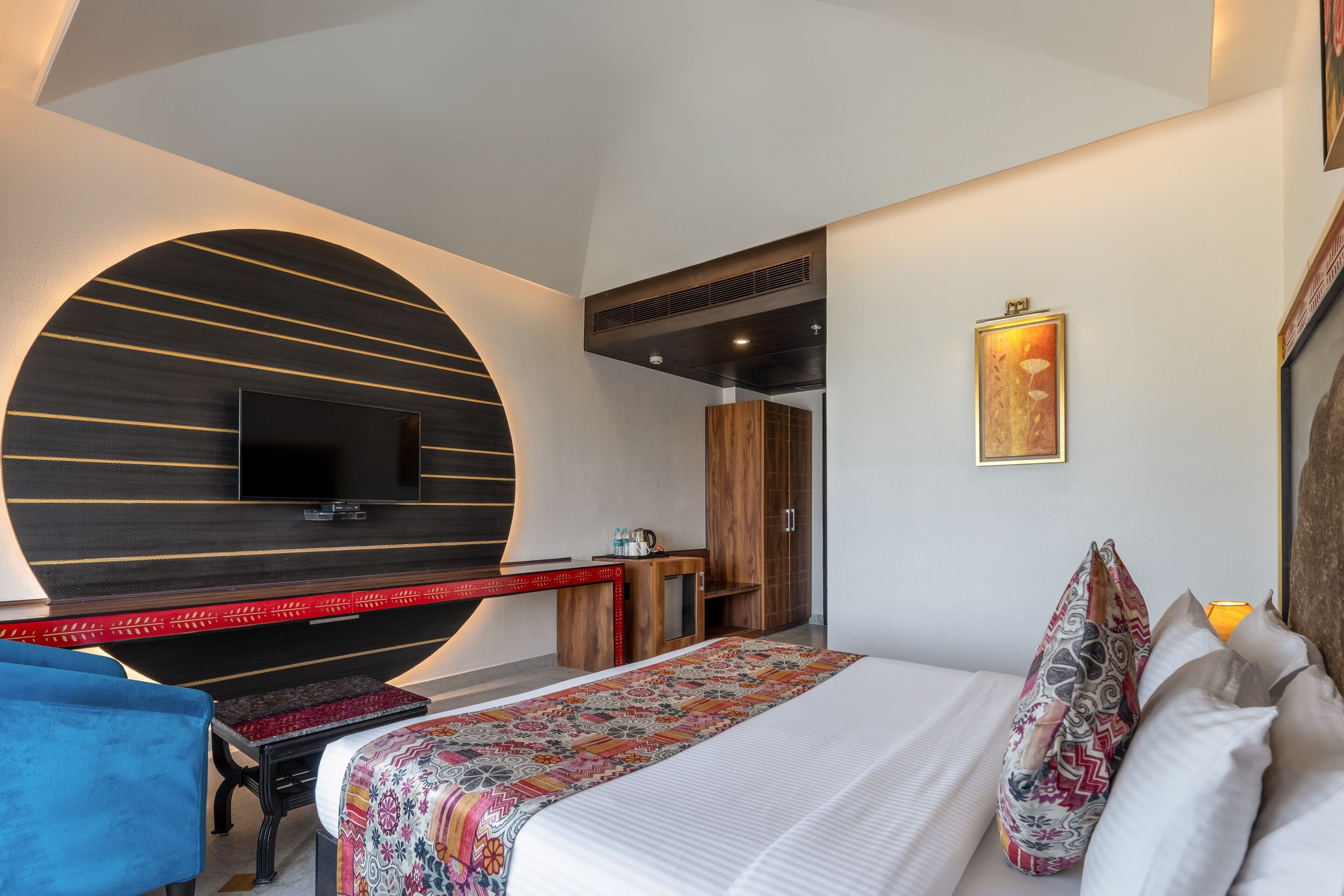 Ein modernes Hotelzimmer mit einem großen Bett, einem Flachbildfernseher an einer gewölbten Wand, einem Holztisch und einem Kleiderschrank.