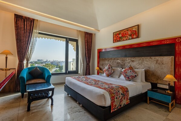 A hotel room with a large bed, a chair, a nightstand, and a window with curtains. - Sterling Balicha Udaipur (Udaipur)