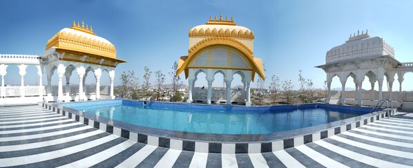 A pool area with ornate white and gold structures, a clear blue sky, and a distant cityscape.