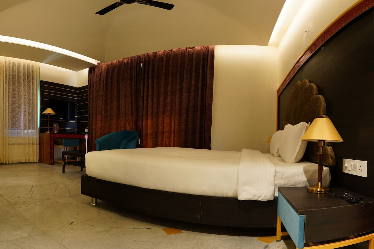 A hotel room with a bed, a desk, a chair, a ceiling fan, and a lamp.