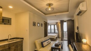 Ein modernes Wohnzimmer mit einer Couch, einem Couchtisch und einem Fernseher. Es gibt eine Küchenzeile mit Spüle und Schränken. Das Zimmer verfügt über ein großes Fenster und einen Balkon.