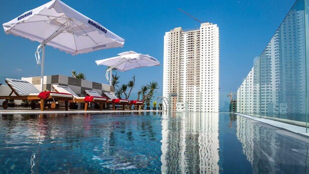 Ein Pool mit Liegestühlen und Sonnenschirmen, umgeben von Hochhäusern.