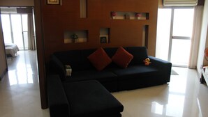 A modern living room with a black sectional sofa, a small table, and decorative items on shelves. - Ploenchit Superb Location, 86sqm, nearby Bumrungrad Hospital - minimum 30 days (Khwaeng Makkasan)