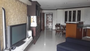 A modern living room with a flat-screen TV, a coffee table, and a sofa. There is a kitchen area with a dining table and chairs. - Ploenchit Superb Location, 86sqm, nearby Bumrungrad Hospital - minimum 30 days (Khwaeng Makkasan)