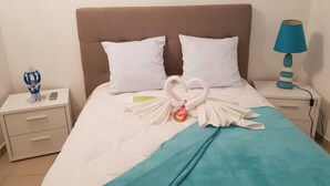 Un llit ben fet amb llençols i manta blancs i color esmeralda, amb dos almoiners blancs i una tovallola decorativa amb forma de cigne. Hi ha una petita làmpada blava sobre la tauleta de nit al costat del llit.