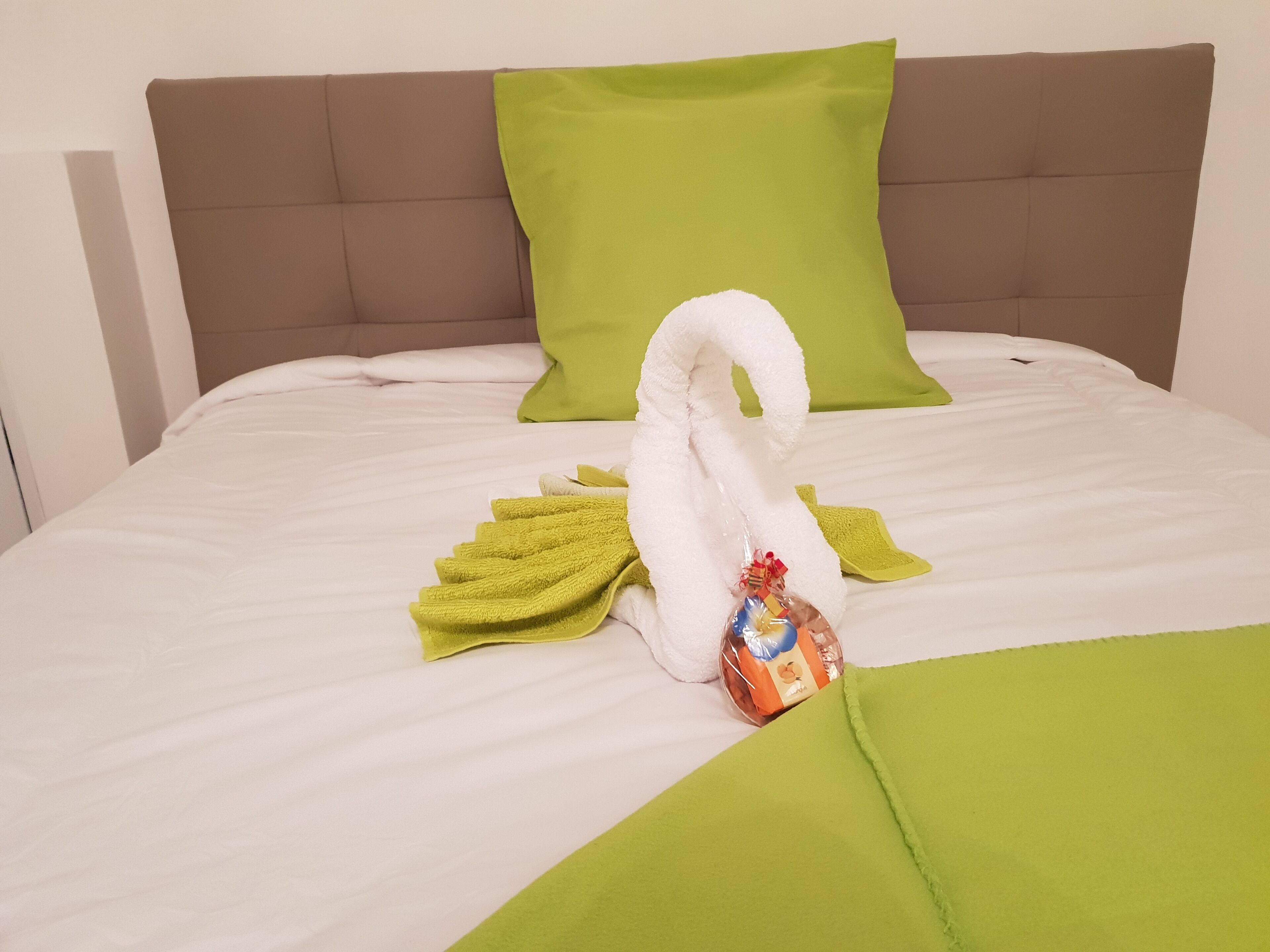 Cama bem arrumada com toalha em formato de cisne, toalhas verdes e cesta de presentes.
