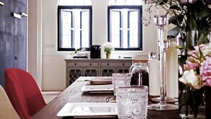 A dining area with a wooden table set for two, a vase of flowers, and a view of a kitchen through arched windows. - Madam's mansion Homestay (Taitung)