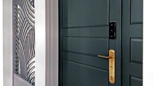 A dark-colored door with a brass handle and a keyhole, adjacent to a decorative glass panel with a geometric pattern. - Madam's mansion Homestay (Taitung)