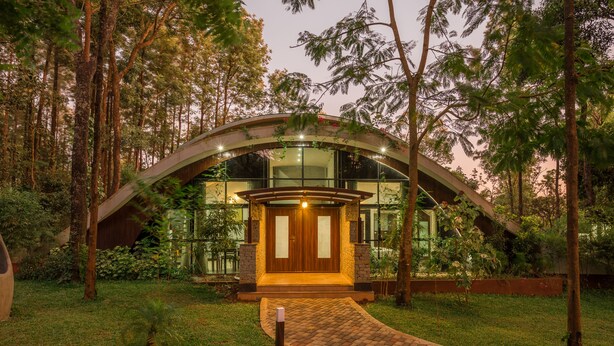 A modern house with a curved roof, surrounded by trees and a brick pathway leading to the entrance. - Siri Nature Roost (Chikkamagaluru)