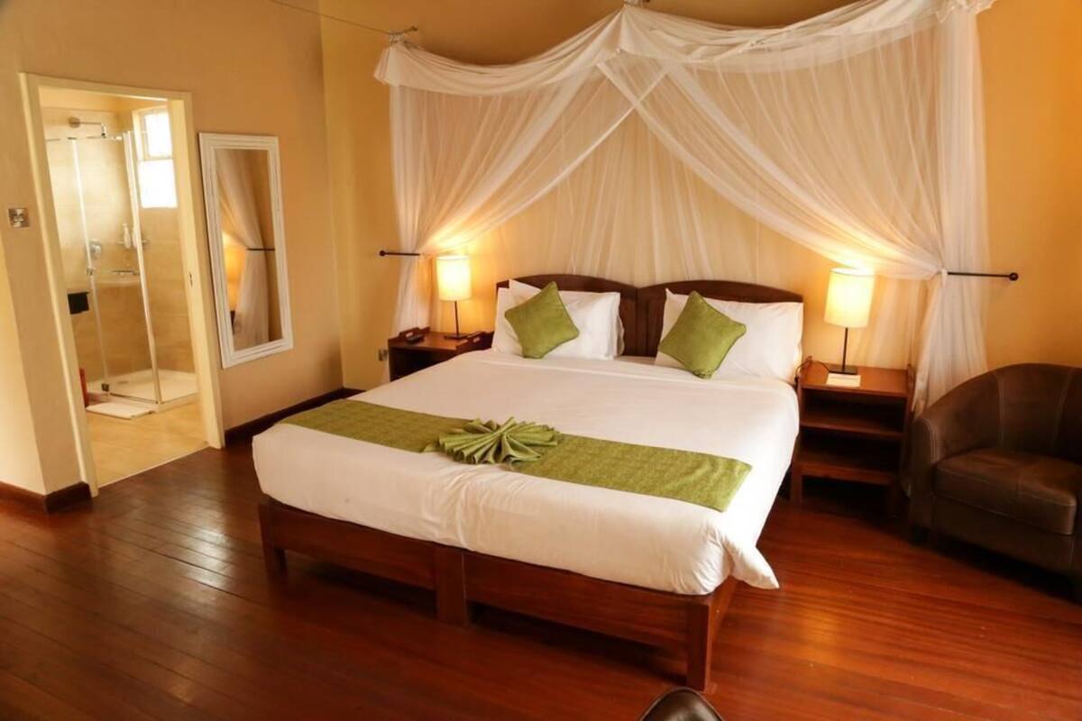 A hotel room with a bed, a nightstand, a chair, a mirror, and a door leading to a bathroom.