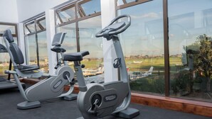 Une salle de sport intérieure équipée de vélos d’appartement et dotée d’une grande fenêtre donnant sur un paysage urbain.