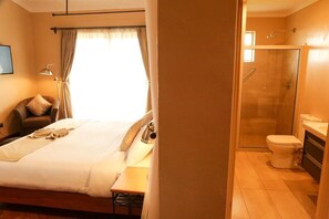 A hotel room with a bed, a chair, a desk, a lamp, a shower, and a toilet. - Aero Club of East Africa (Nairobi)