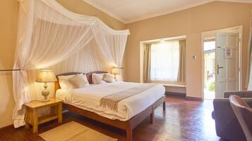 A bedroom with a large bed, bedside lamps, a bedside table, a window with curtains, and a door.