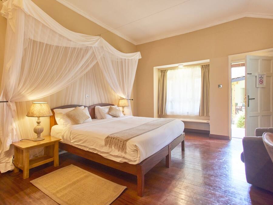 A bedroom with a large bed, bedside lamps, a bedside table, a window with curtains, and a door.