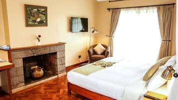 A hotel room with a fireplace, a bed, a chair, a TV, and a window with curtains.